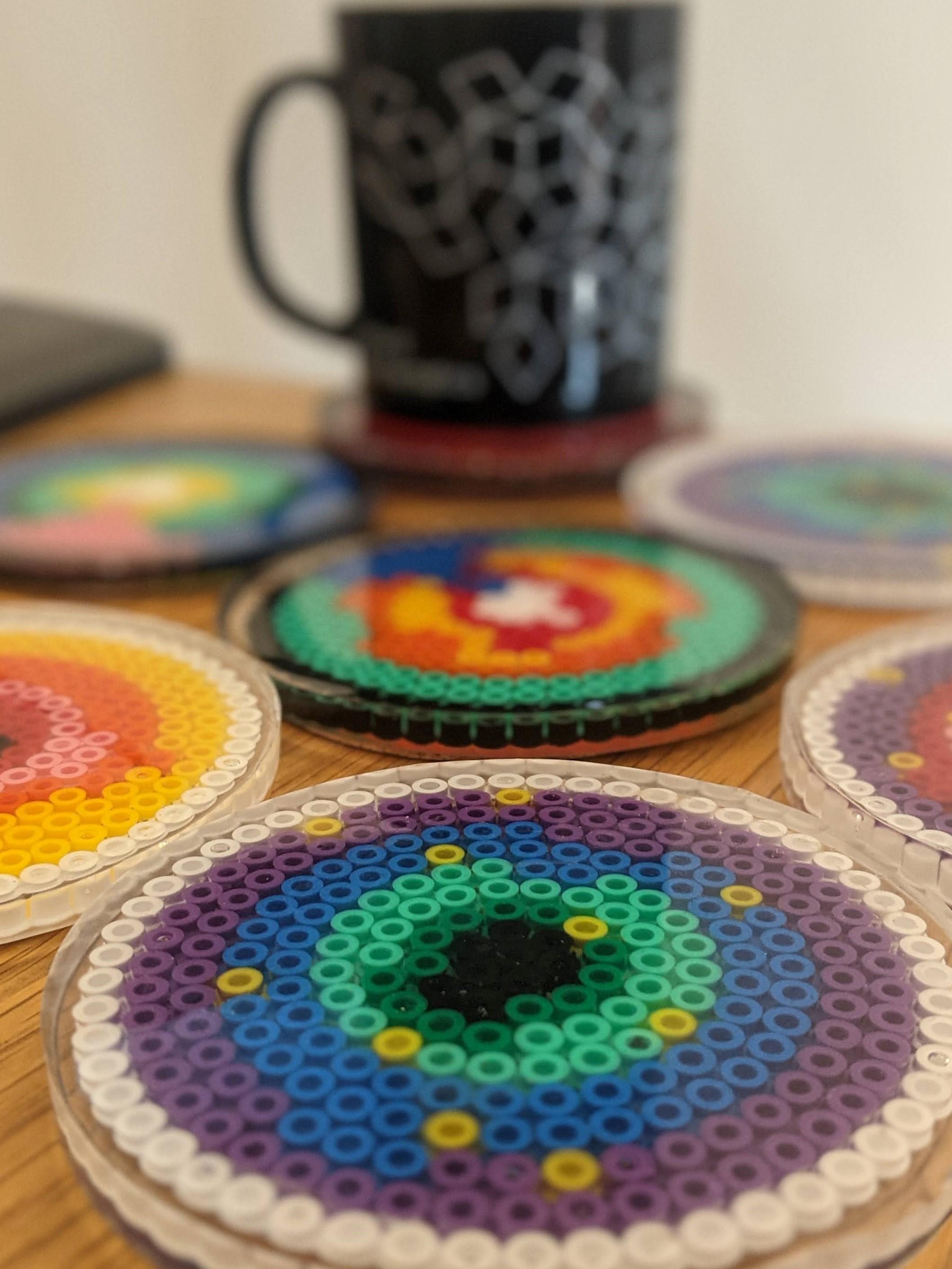 Coasters made from plastic beads in resin, showing show an agent-based model of microbeads infiltrating a tumour spheroid.
