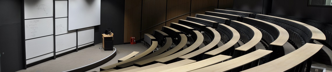 A large lecture room with many white boards and banked seating