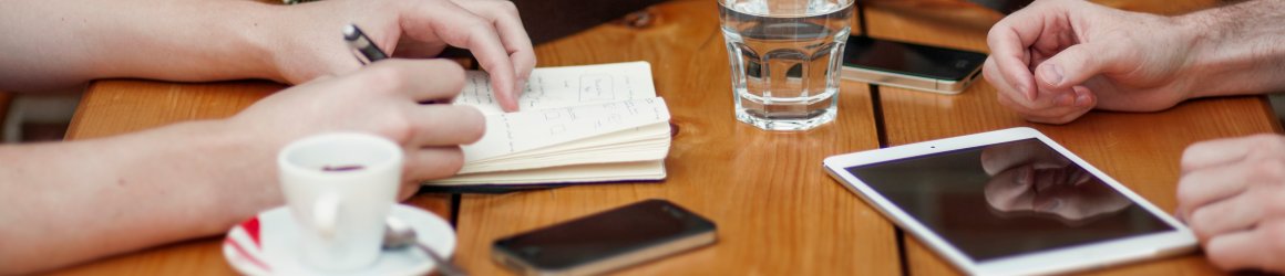 view of a table top with notebooks, tablet and bag as people collaborate