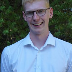 A photo of Elliott Hughes, a white male with red hair and glasses who is smiling.