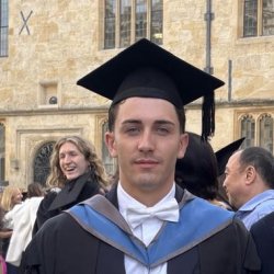Graduate wearing academic dress and a mortarboard outside an Oxford college.