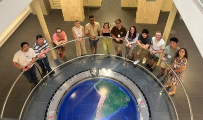 Students stand in a semicircle around a model globe, looking up at the camera Students stand in a semicircle around a model globe, looking up at the camera