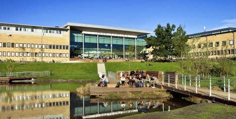 A courtyard with a human-made pond, decking with students relaxing, and green space. The modern concrete/glass university building encloses the courtyard A courtyard with a human-made pond, decking with students relaxing, and green space. The modern concrete/glass university building encloses the courtyard