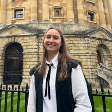 Girl in official university attire in front of library.