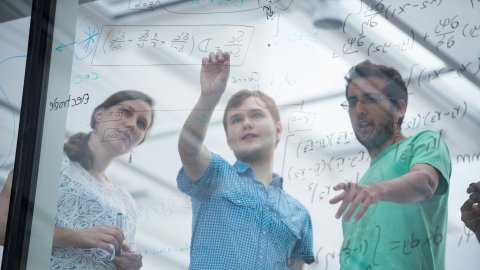 3 students working on maths on a glass board