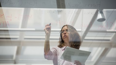 Female student writing mathematical formulae on glass
