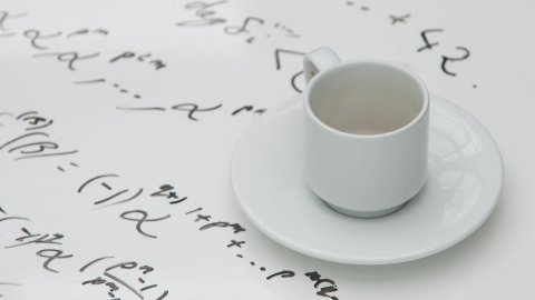 Tea cup sitting on table with mathematical formulae written on table top