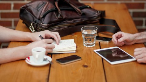 view of a table top with notebooks, tablet and bag as people collaborate