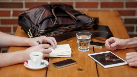 view of a table top with notebooks, tablet and bag as people collaborate